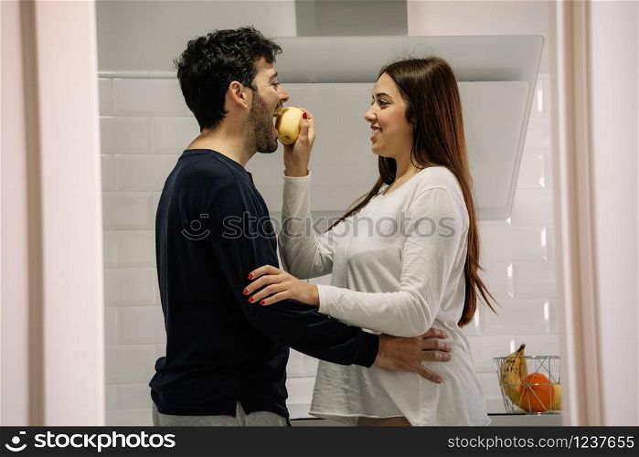 young woman giving her husband an apple in the kitchen