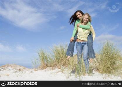 Young woman giving piggyback ride to her friend on a sand hill