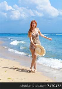 Young woman goes on ocean coast with hat