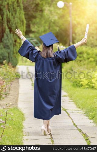 Young woman graduate put her hands up and celebrating with certificate in her hands and feeling so happiness in