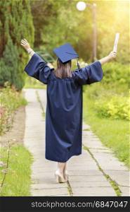Young woman graduate put her hands up and celebrating with certificate in her hands and feeling so happiness in