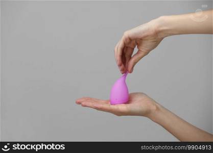 Young woman hand holding a pink menstrual cup - gray background. Gynecology concept.. Young woman hand holding a pink menstrual cup - gray background. Gynecology concept