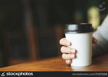 young woman hand holding paper cup of take away drinking coffee hot on the table wooden in cafe coffee shop.