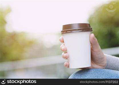 young woman hand holding paper cup of take away drinking coffee on natural morning sunlight refreshing. space Place for your text or logo.