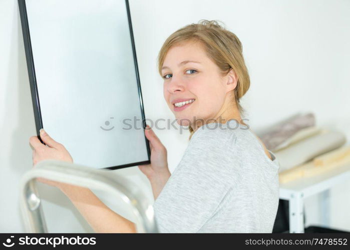 young woman hanging a picture on the wall