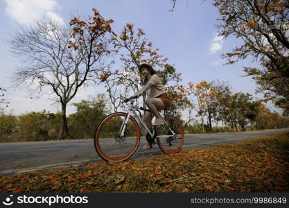 Young woman happy enjoying the outdoor leisure activity riding a bike and smiling for happiness the healthy lifestyles at full of beautiful orange flower background, The concept of travel and freedom