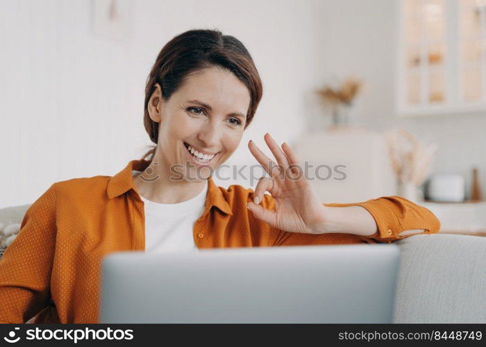 Young woman has video call and shows ok. European girl has online conference at home. Freelancer or businesswoman with computer is talking at internet meeting. Remote work on quarantine.. Young woman has video call and shows ok. Freelancer or businesswoman working on quarantine.