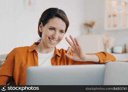 Young woman has video call and shows ok. European girl has online conference at home. Freelancer or businesswoman with computer is talking at internet meeting. Remote work on quarantine.. Young woman has video call and shows ok. Freelancer or businesswoman working on quarantine.