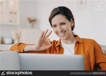 Young woman has video call and shows ok. European girl has online conference at home. Freelancer or businesswoman with computer is talking at internet meeting. Remote work on quarantine.. Young woman has video call and shows ok. Freelancer or businesswoman working on quarantine.