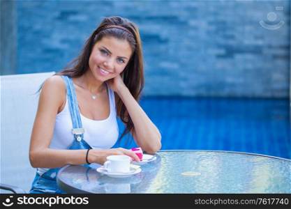 Young woman having a breakfast with coffee and cake sitting outdoors in a cafe and smiling. Woman with coffee and cake in cafe