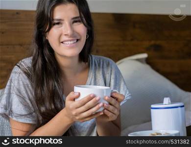 Young woman having breakfast and holding cup of coffee at home in bed. Lifestyle concept.