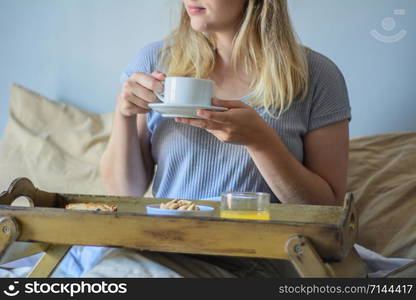 Young woman having breakfast and holding cup of coffee at home in bed. Lifestyle concept.