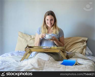 Young woman having breakfast and holding cup of coffee at home in bed. Lifestyle concept.