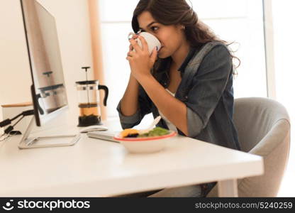 Young woman having breakfast on the computer desk