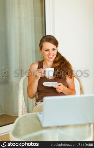 Young woman having coffee and looking in laptop on terrace