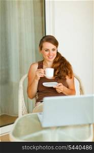Young woman having coffee and looking in laptop on terrace