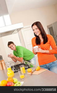 Young woman having coffee in the kitchen, man in background