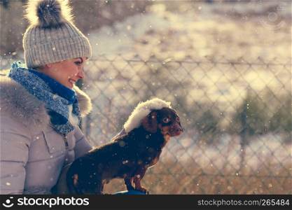 Young woman having fun during winter. Female playing with her small purebreed dachshund dog puppy while snow is snowing. Woman playing with dog during winter