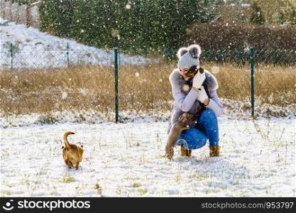 Young woman having fun during winter. Female playing with her three small purebreed dogs puppies while snow is snowing. Woman playing with dogs during winter