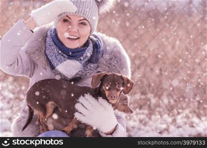 Young woman having fun during winter. Female playing with her two small purebreed dogs puppies while snow is snowing. Woman playing with dogs during winter