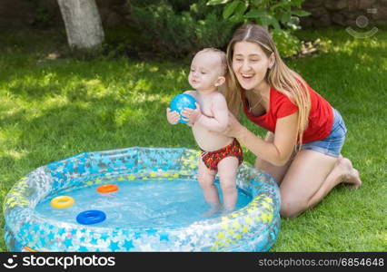 Young woman having fun with her baby boy in swimming pool at backyard