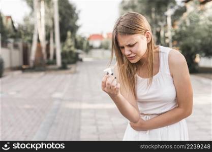young woman having stomach ache holding white pills bottle