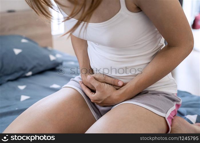 Young woman having stomach ache on the bed. Periods cramp problems concept. Young woman having stomach ache on the bed
