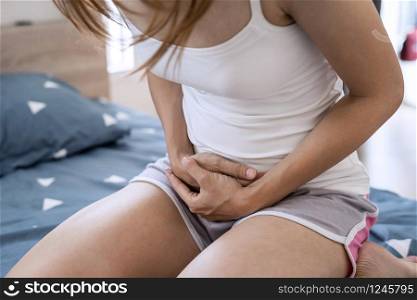 Young woman having stomach ache on the bed. Periods cramp problems concept. Young woman having stomach ache on the bed