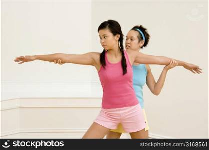 Young woman helping another young woman with positioning on her yoga pose.