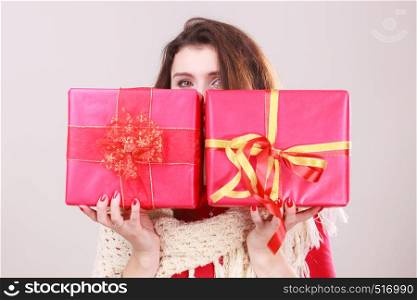 Young woman hiding her face behind presents two gift boxes with ribbon. Christmas season celebration concept.. Woman holds red christmas gift boxes