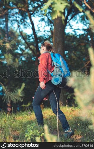 Young woman hiker with backpack walking along the path through the forest during summer vacation trip