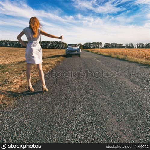 young woman hitch-hiking on a road at the fields