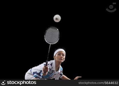 Young woman hitting shuttlecock with badminton racket isolated over black background