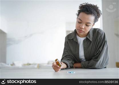 Young woman hold bottle with pills read medicine instruction before take meds. Pensive girl holding medicines thinking of taking medications, doubt whether to take tablets, sitting at table.. Pensive young woman holds bottle with medicines doubt whether to take pills. Healthcare. Copy space