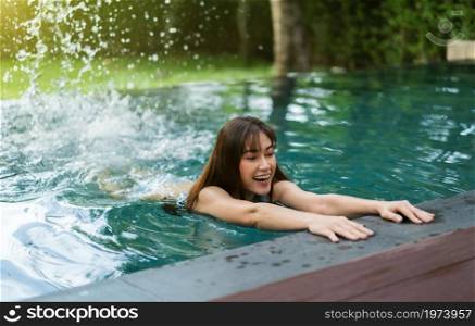 young woman hold on to the edge of the swimming pool and splashing water with her feet