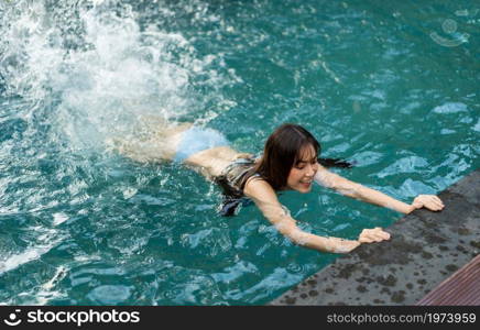 young woman hold on to the edge of the swimming pool and splashing water with her feet