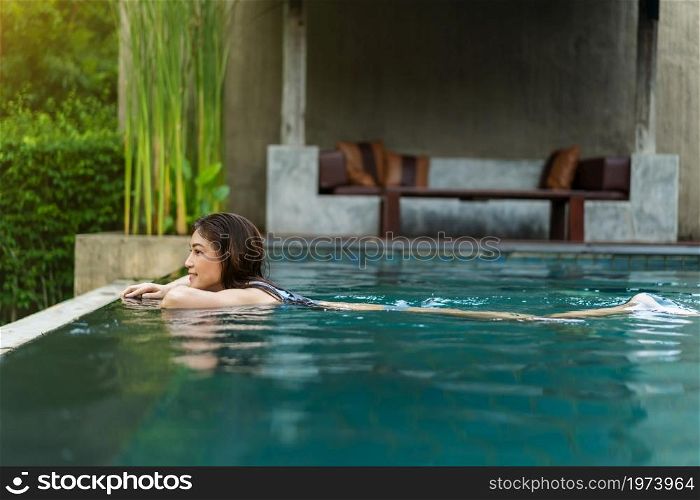 young woman hold on to the edge of the swimming pool and splashing water with her feet