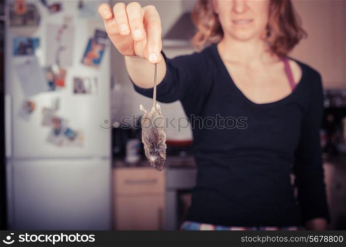 Young woman holding a dead mouse by it&rsquo;s tail in her kitchen