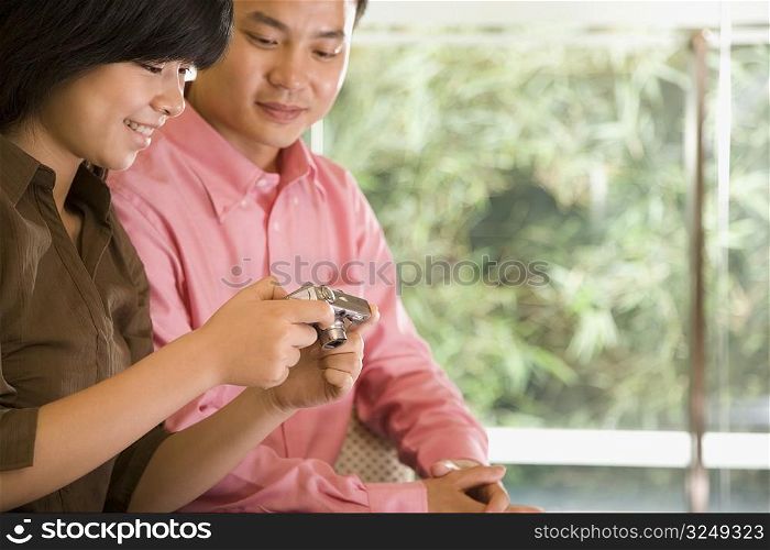Young woman holding a digital camera with a young man sitting beside her