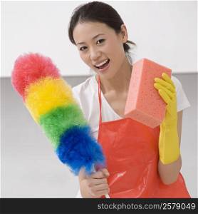 Young woman holding a duster and a bath sponge