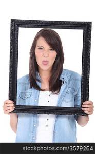 young woman holding a picture frame and sticking out her tongue
