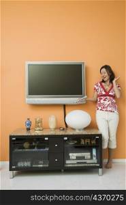 Young woman holding a remote control and standing near a cabinet