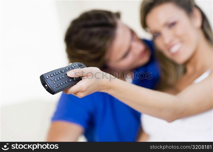 Young woman holding a remote control with a young man kissing her