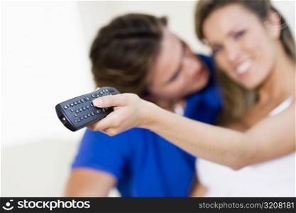Young woman holding a remote control with a young man kissing her