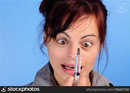 young woman holding a syringe and looking funny . Focus is on the woman.