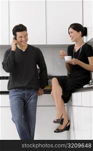 Young woman holding a tea cup with a young man talking on a mobile phone