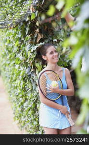 Young woman holding a tennis ball and a tennis racket smiling