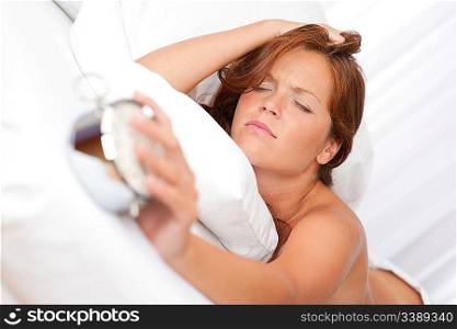 Young woman holding alarm clock, lying in white bed