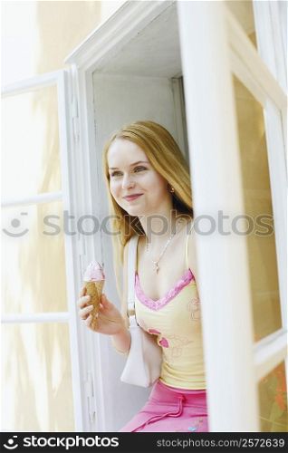 Young woman holding an ice-cream cone and sitting in a window