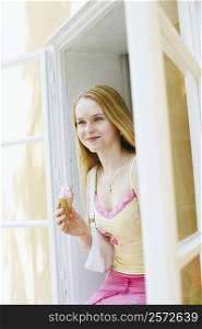 Young woman holding an ice-cream cone and sitting in a window